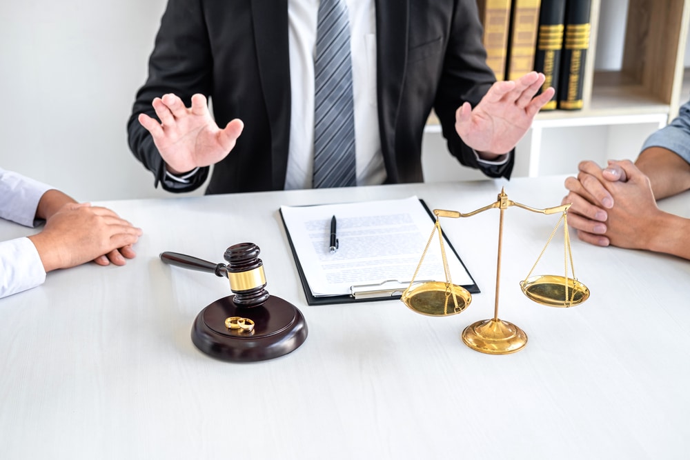 Médiateur en costume avec balance, marteau de justice et alliances lors d'une procédure de divorce ou séparation.