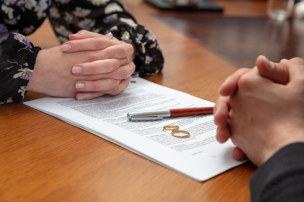 Alliances et stylo sur une demande de divorce avec mains jointes de deux personnes sur une table en bois.